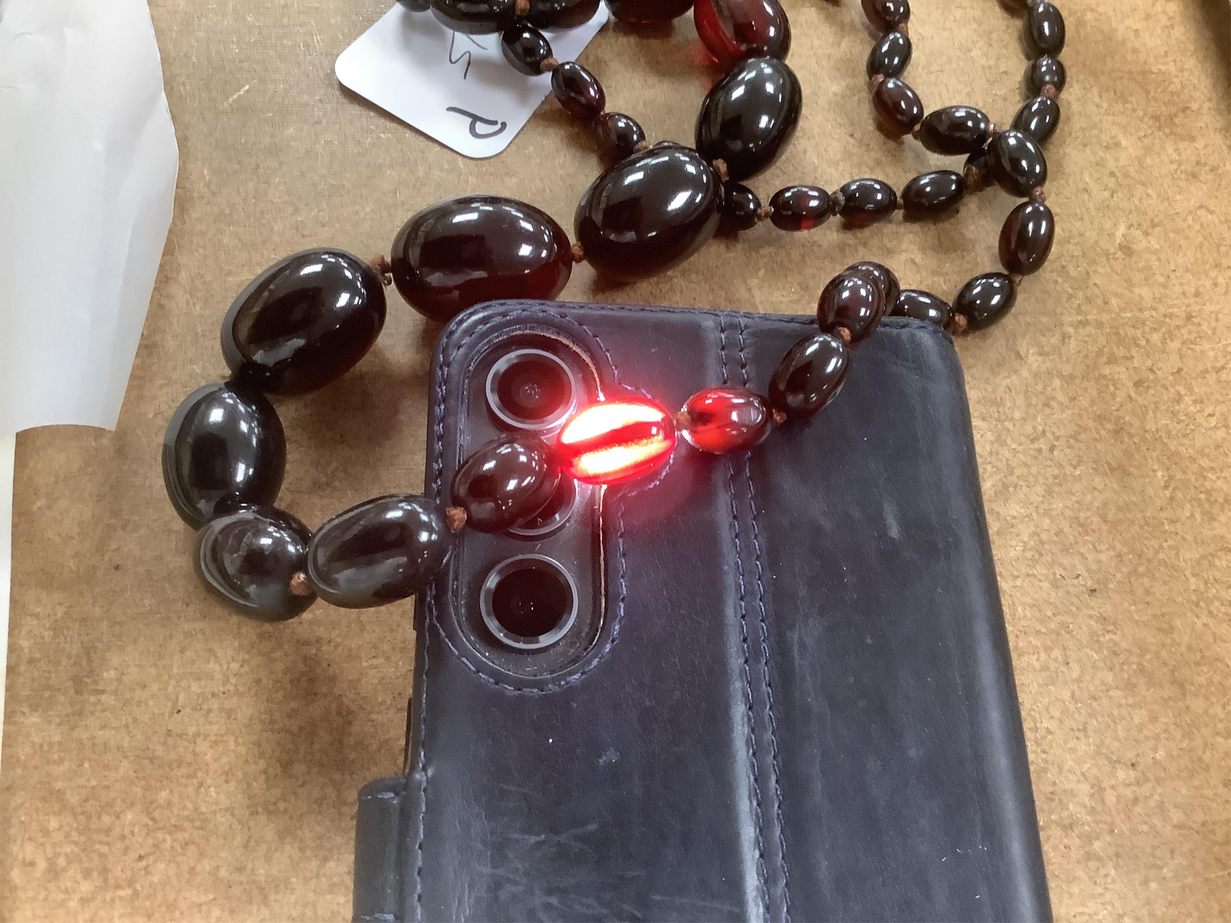 A single strand graduated simulated oval dark cherry amber bead necklace, 110cm, gross weight 90 grams.